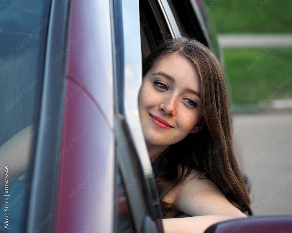 Young, beautiful girl at the wheel of the car. The girl looks in the rearview mirror and smiles. The girl has freckles. woman driver