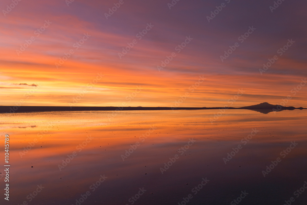 Naklejka premium 雲と山のシルエットが水面に反射するウユニのサンセット。Uyuni gradational sunset, clouds and mountain silhouette reflected surface of the water.
