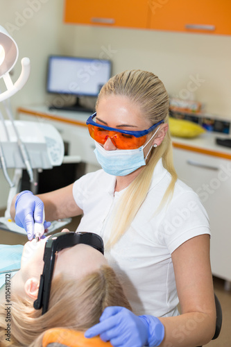 Woman dentist in mask filling tooth