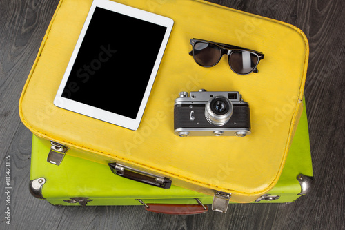 Slika na platnu Sunglasses, vintage camera and tablet on yellow valise on dark background
