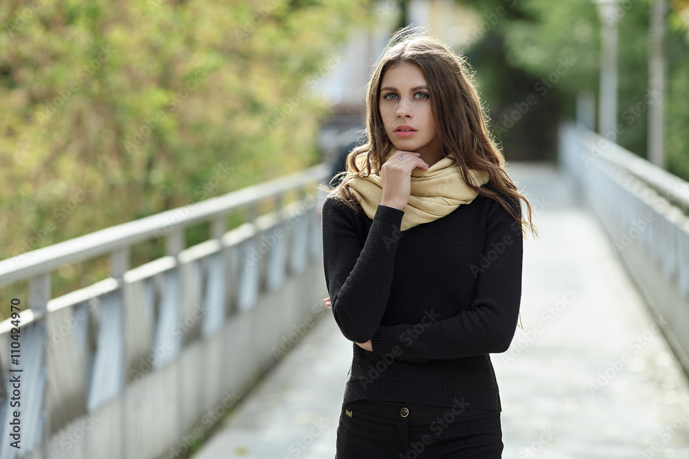 Outdoor portrait of young beautiful brunette woman with wavy long hair stares into camera posing on the park bridge