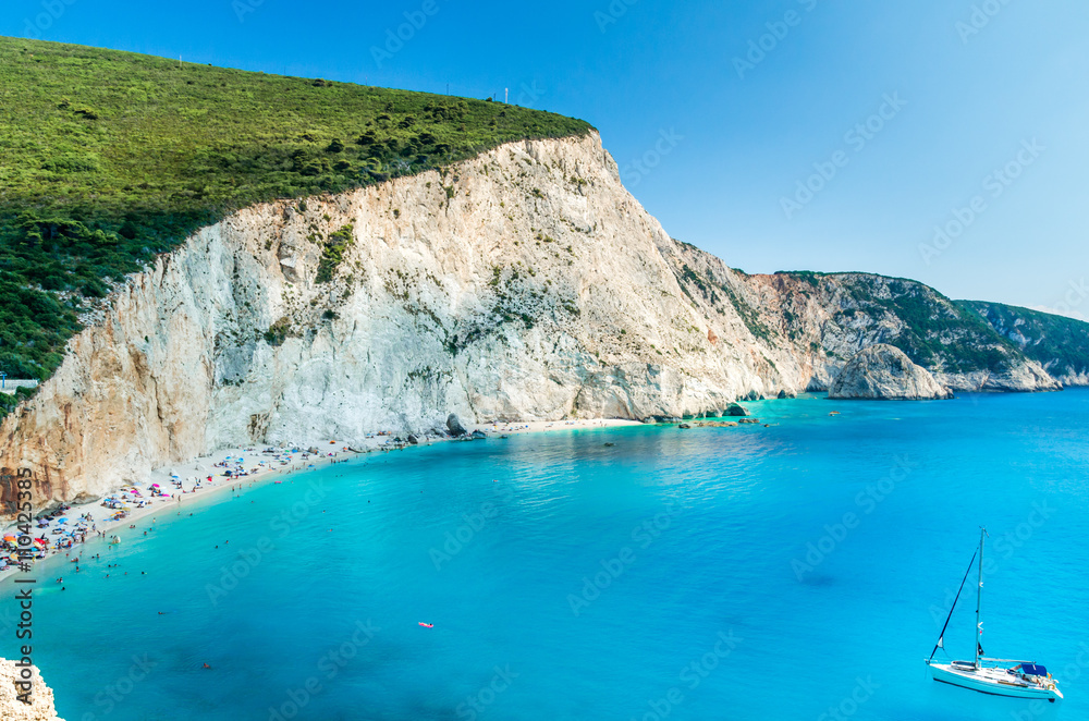 Porto Katsiki beach in Lefkada island, Greece. Beautiful view over the beach. The water is turquoise and there are tourists on the beach and a boat on the sea. Porto Katsiki beach in Lefkada island, Greece. Beautiful view over the beach. The water is turquoise and there are tourists on the beach and a boat on the sea.