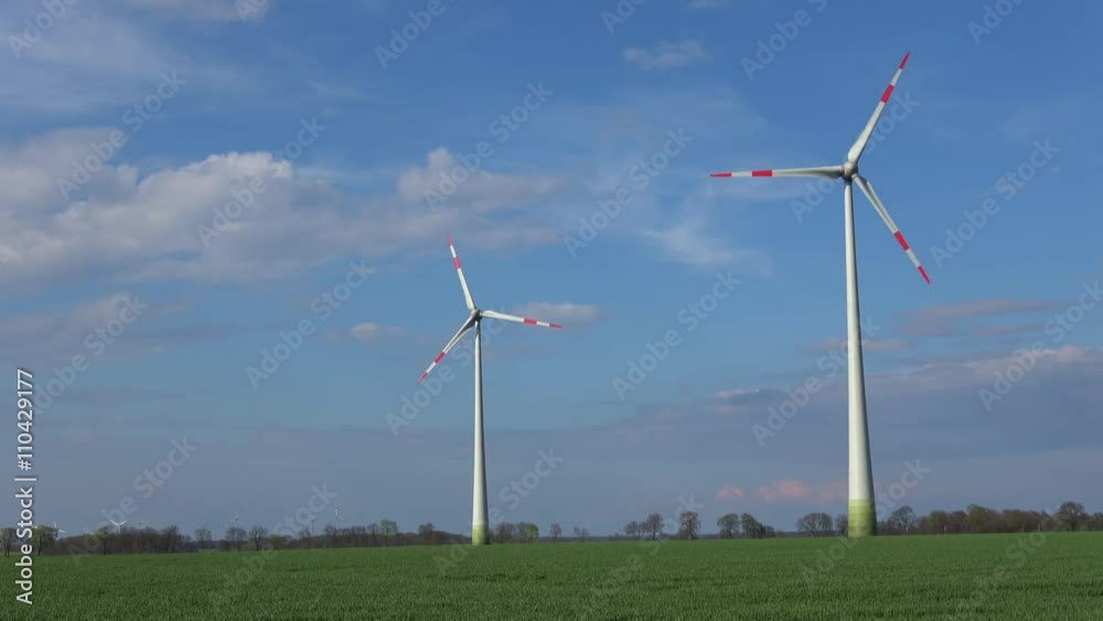 Windräder stehen auf einem Feld, drehen sich und produzieren Strom Windräder stehen auf einem Feld, drehen sich und produzieren Strom