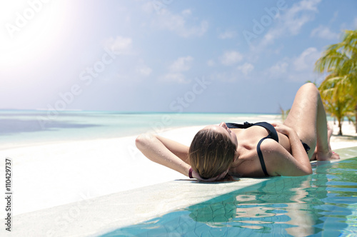 Woman sunbathing laying on her back relaxing by the pool in trop