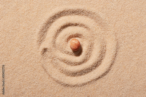 Photography Spiral drawn on beach sand with pink round sea stone in centre