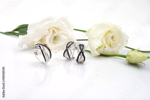 Jewelry ring and earrings with diamonds next to flowers on white photo