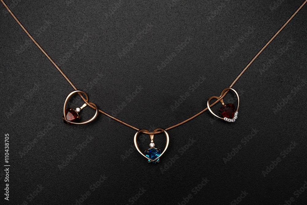 Gold heart-shaped pendants with colored topazes on black backgro Gold heart-shaped pendants with colored topazes on black backgro