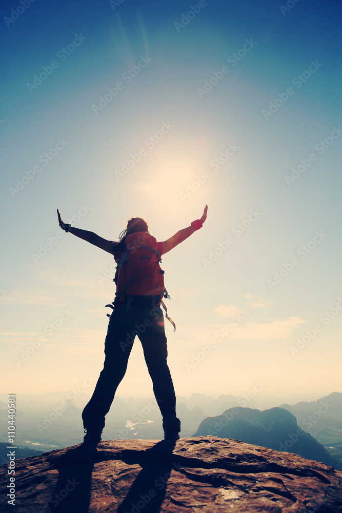 silhouette of young successful woman hiker open arms on mountain peak