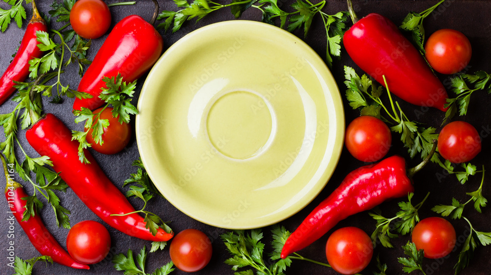 Fresh chili peppers, herbs around green plate on black background Fresh chili peppers, herbs around green plate on black background