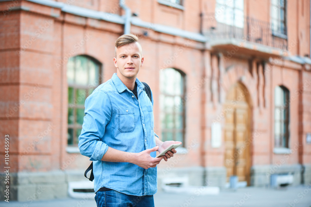 Fototapeta premium Portrait of a student in a denim shirt while holding a tablet on the background of the educational task of brick