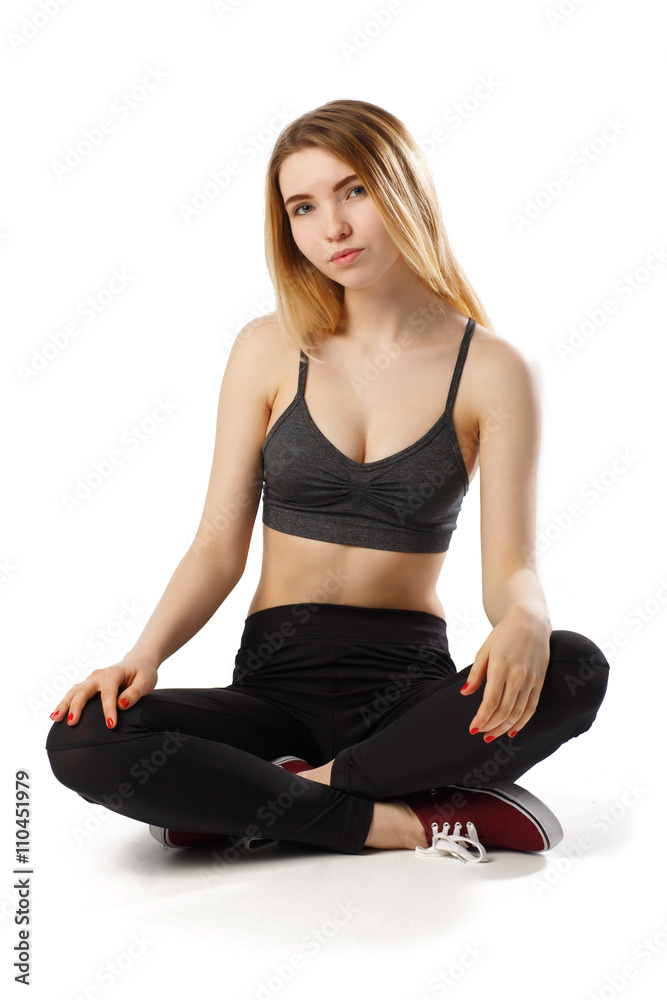 Portrait of attractive cheerful fitness girl in gray top and black leggings posing over white background isolated sit on the floor