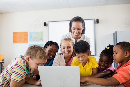 Happy teacher and pupils using laptop © WavebreakMediaMicro