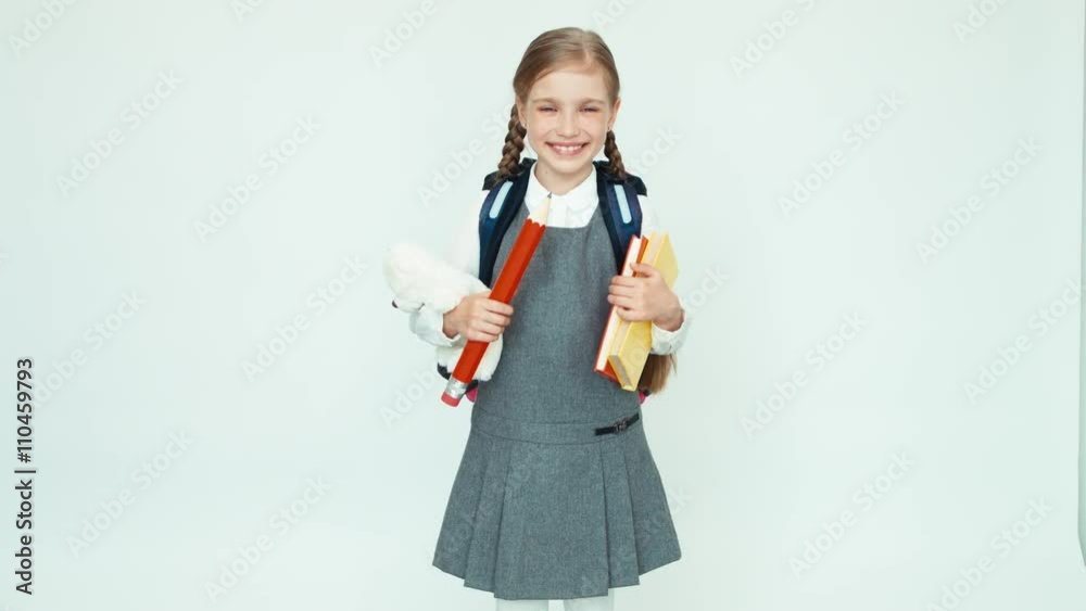 Cute schoolgirl 7-8 years with backpack holding books and big pencil and teddy bear and smiling at camera on white Cute schoolgirl 7-8 years with backpack holding books and big pencil and teddy bear and smiling at camera on white
