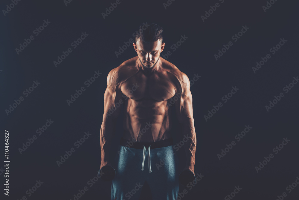Closeup of a muscular young man lifting dumbbells weights on dar