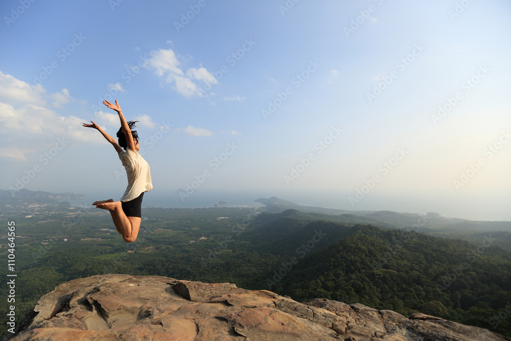 cheering young asian woman jumping on mountain peak rock