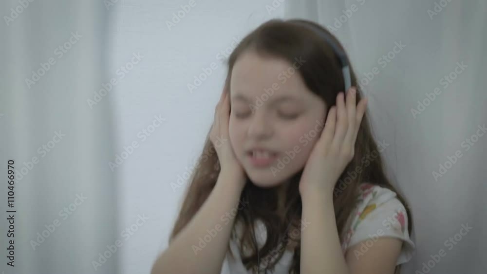 Beautiful little girl in headphones singing a song emotionally and dancing at window. Beautiful little girl in headphones singing a song emotionally and dancing at window.