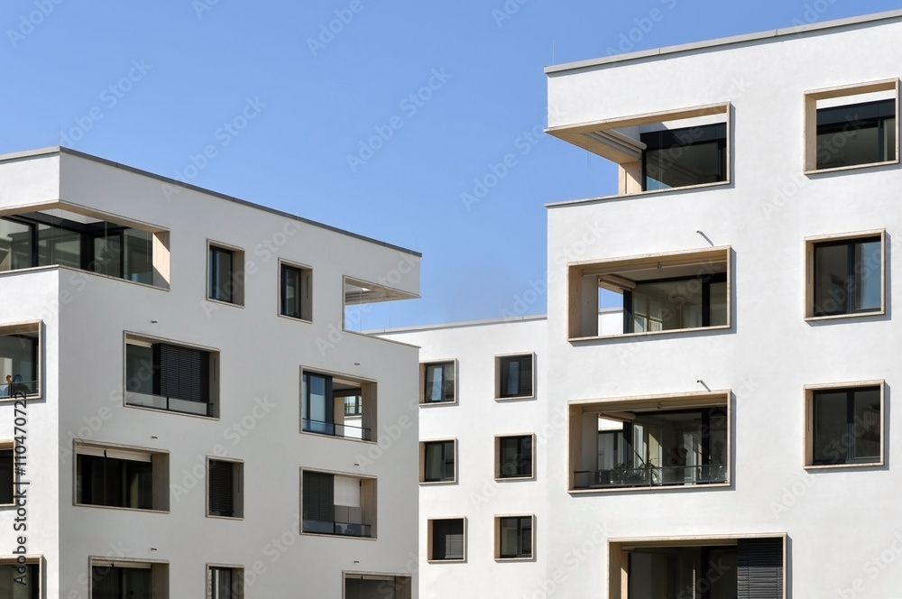 Fragment of white residential buildings with balconies and rectangular windows on a background of blue sky.