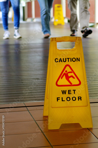 Warning sign for slippery floor with people legs in the backgrou