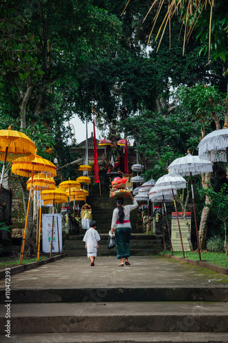 Balinese woman with son going to the temple with ceremonial box on her head during Balinese New Year or Nyepi Day celebrations on in Ubud, Bali.