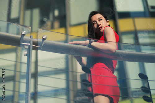 Beautiful Asian girl model in red dress posing at the modern music note style city background.