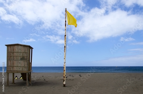 Lifeguard tower with yellow flag waving over the blue skyon the beach