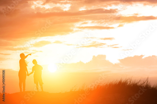 silhouette mother and son at sunset , pointing at the sun © Johnstocker