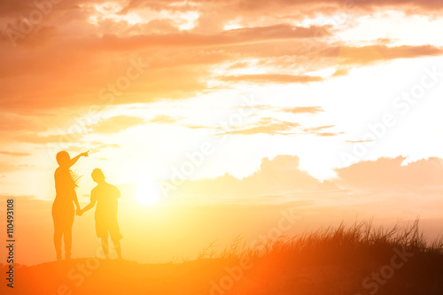 silhouette mother and son at sunset , pointing at the sun