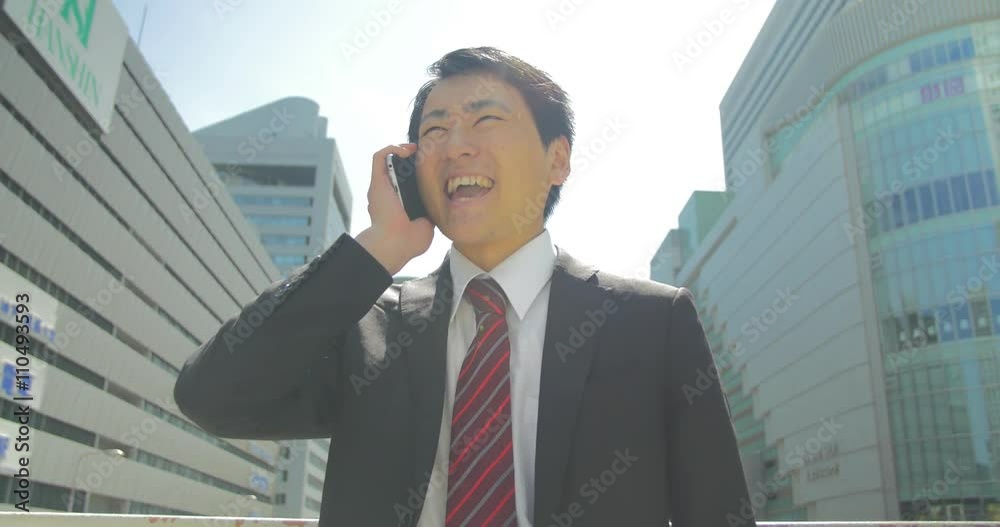 Confident young Japanese business man takes positive phone call and celebrates in city Confident young Japanese business man takes positive phone call and celebrates in city