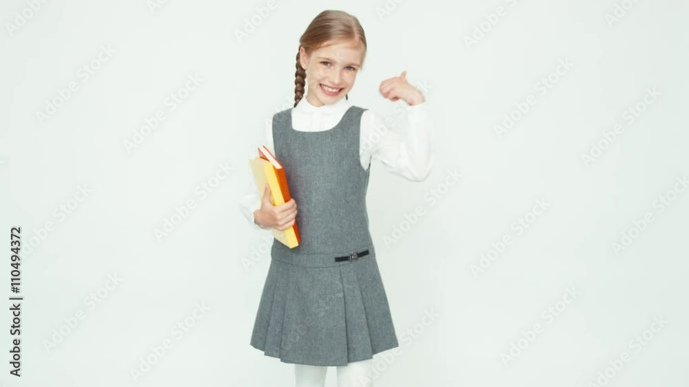 Portrait schoolgirl 7-8 years holding books turns around at camera on white background and smiling at camera with teeth Portrait schoolgirl 7-8 years holding books turns around at camera on white background and smiling at camera with teeth