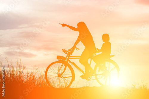 Silhouette of mother and daughter biking at sunset happy time