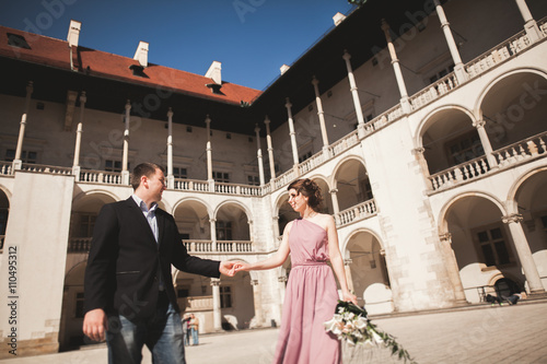 Beautiful couple, man, girl with long pink dress posing in old castle near columns. Krakow Vavel