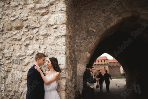 Gorgeous wedding couple, bride, groom kissing and hugging near wall