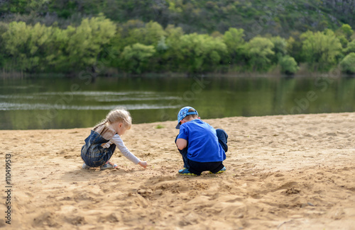 Brother and sister playing on sand near river