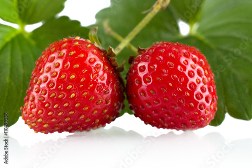 Two whole strawberries with leaves on a white