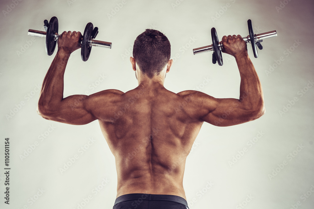 Muscular bodybuilder guy doing exercises with dumbbells over grey background with copyspace Muscular bodybuilder guy doing exercises with dumbbells over grey background with copyspace