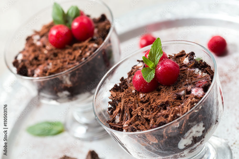 Chocolate desserts with whipped cream and cherries in glasses,light grey background, selective focus, close up Chocolate desserts with whipped cream and cherries in glasses,light grey background, selective focus, close up
