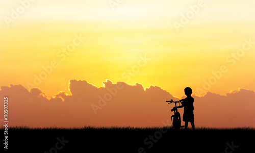 Silhouette of little boy standing hold bicycle sunset background © napatcha
