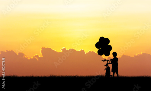 Silhouette of little boy standing hold bicycle sunset background