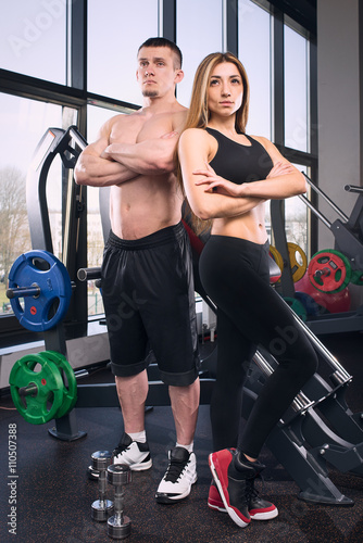 Muscular man and beauty girl posing near the window in gym
