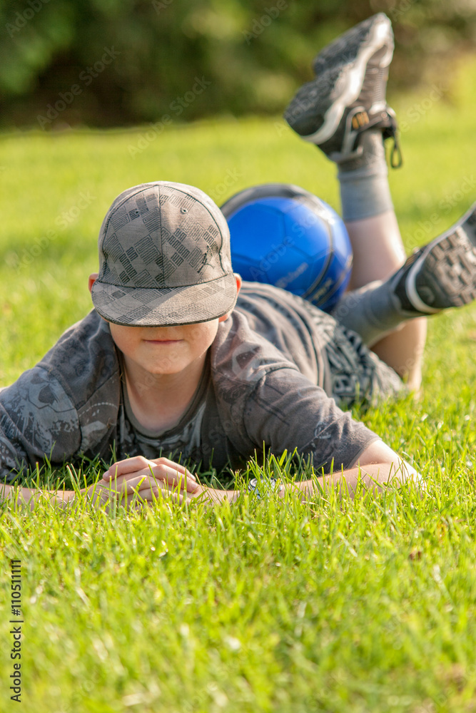 Young boy laying on grass, legs up and a soccer ball on his legs. Young boy laying on grass, legs up and a soccer ball on his legs.