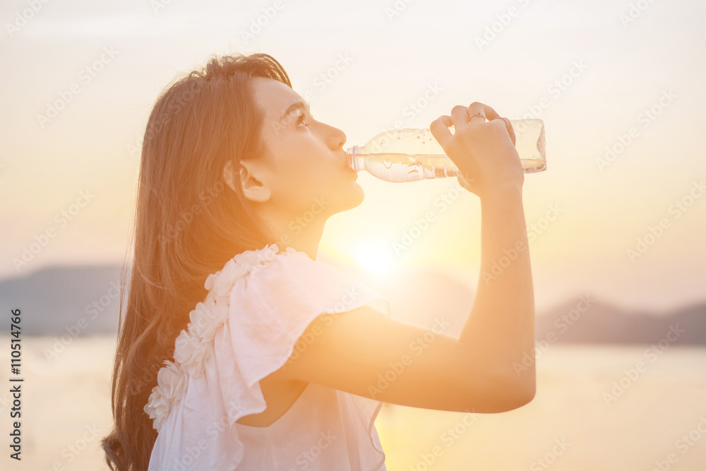 Fototapeta premium beautiful young woman drinking water with sunrise in the morning