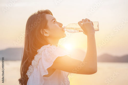 beautiful young woman drinking water with sunrise in the morning