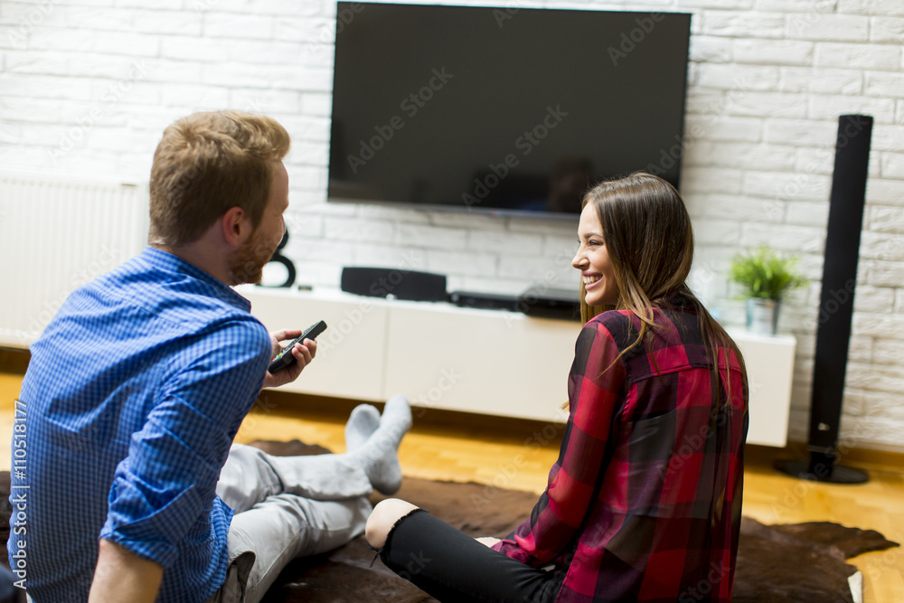 Couple watching television sitting comfortably on floor Couple watching television sitting comfortably on floor