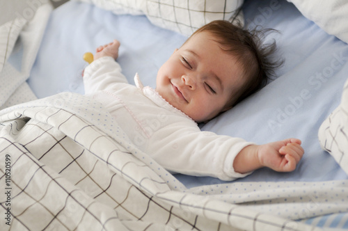 Smiling baby girl lying on a bed sleeping on blue sheets photo