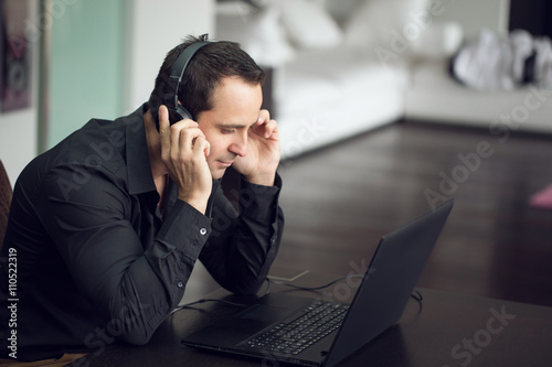 Casual man listening music by headphones and laptop