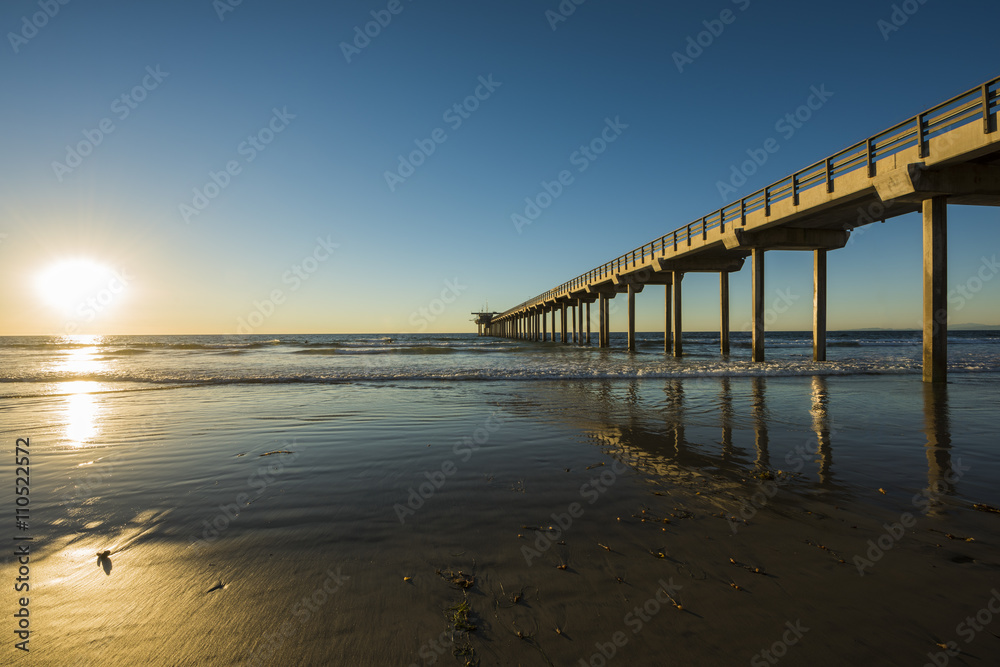 Wide angle shot of Scripps Pier with reflection during sunset with sun in La Jolla, San Diego, California