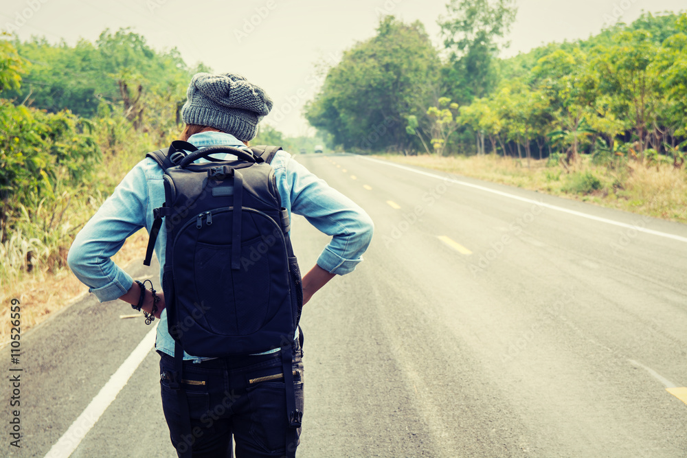 Rear view of a young woman hitchhiking carrying backpack walking