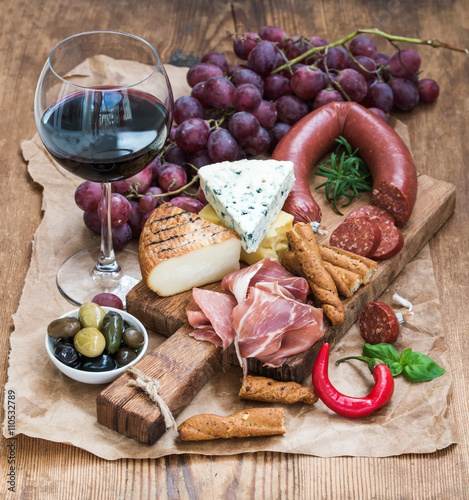 Glass of red wine, cheese and meat board, grapes,fig, strawberries, honey, bread sticks  on rustic wooden table, white background