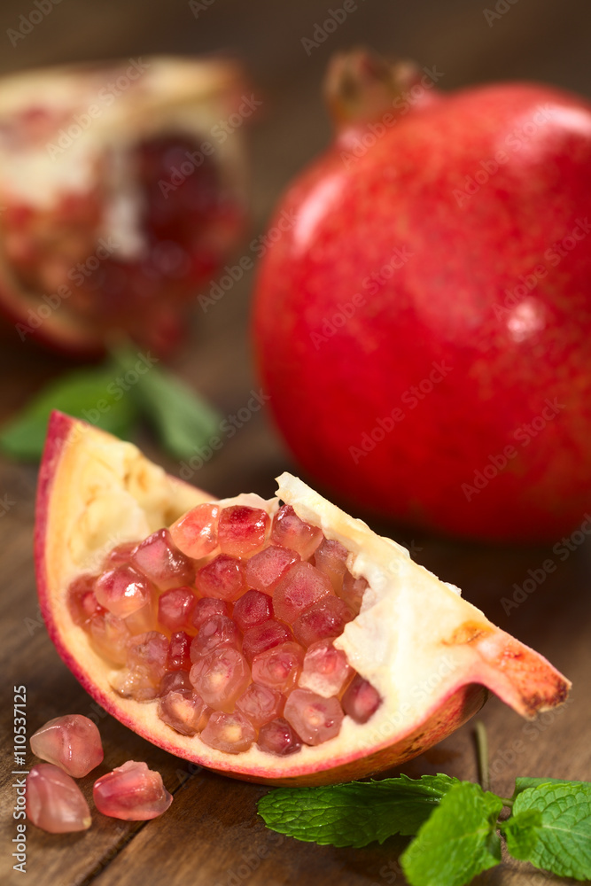 Granatapfelstück (lat. Punica granatum) mit ganzer Granatapfel im Hintergrund (Selektiver Fokus, Fokus auf die oberen Samen) Granatapfelstück (lat. Punica granatum) mit ganzer Granatapfel im Hintergrund (Selektiver Fokus, Fokus auf die oberen Samen)