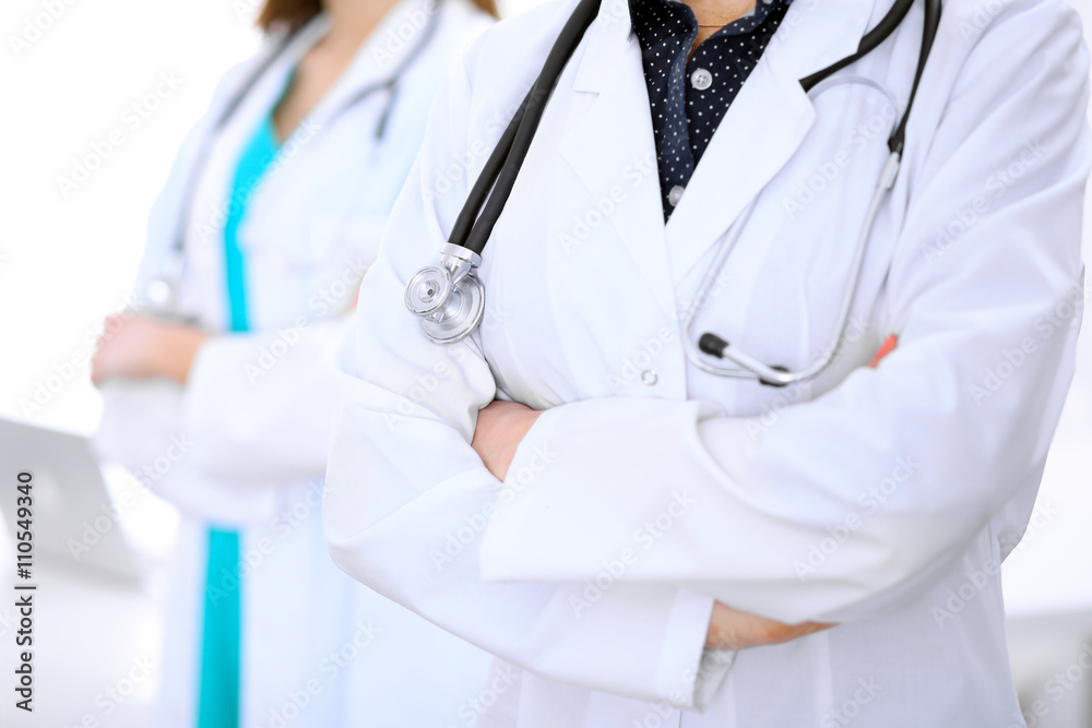 Close up of unknown female doctor standing in a hospital with her colleague in the background Close up of unknown female doctor standing in a hospital with her colleague in the background